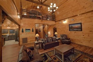 A spacious wooden interior with a high ceiling, a dining area, and a living room furnished with a sofa, armchair, and coffee table. - Smoky Bear Lodge | Private Pool, Mtn Views, Hot Tub, Game Room, Sleeps 10 + Free Attraction Tickets (Wears Valley)