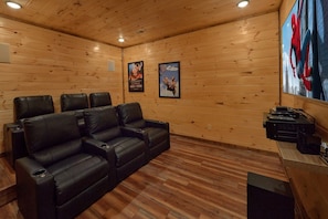 A room with a wooden interior, a black leather sofa, a small table with audio equipment, and two posters on the wall. - Smoky Bear Lodge | Private Pool, Mtn Views, Hot Tub, Game Room, Sleeps 10 + Free Attraction Tickets (Wears Valley)