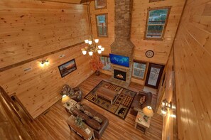 A cabin interior with a fireplace, wooden walls, a television, and a dining area. - Smoky Bear Lodge | Private Pool, Mtn Views, Hot Tub, Game Room, Sleeps 10 + Free Attraction Tickets (Wears Valley)