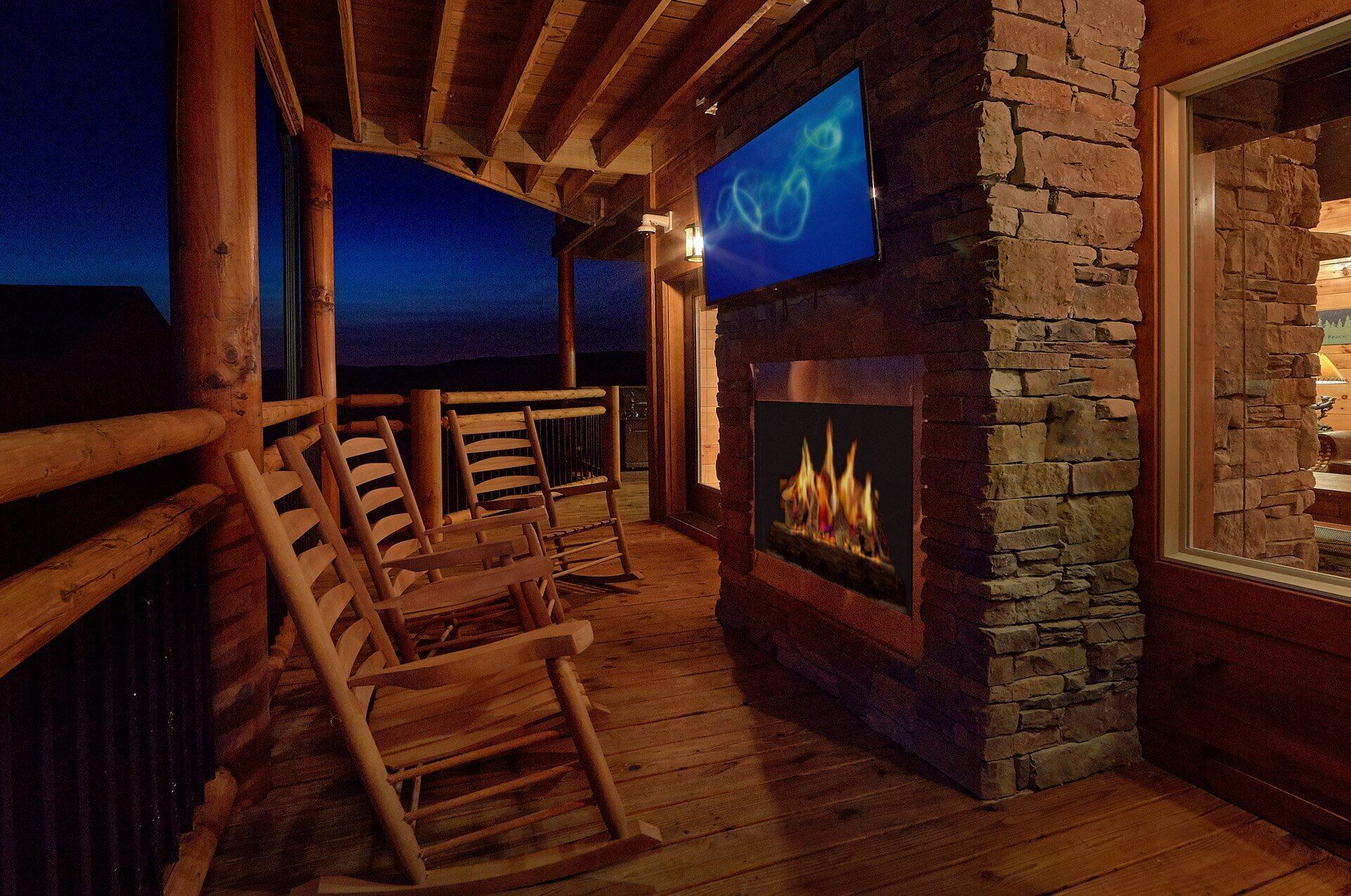 Une terrasse en bois avec une cheminée en pierre, un téléviseur fixé au mur et une vue sur le ciel nocturne.