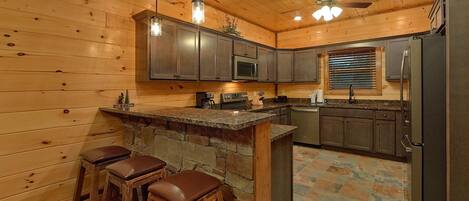 A kitchen with wooden walls, a stone island, bar stools, and a ceiling fan.
