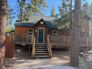 Une cabane en rondins avec un porche à l’avant, une porte verte et un petit escalier menant à l’entrée.