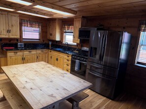 Eine Küche mit Holzschränken, einem Edelstahlkühlschrank, einem eingebauten Backofen und einem Holzessttisch.