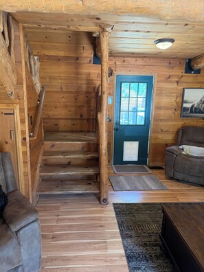 Un intérieur en bois avec un escalier, une porte bleue, un canapé et un tapis.