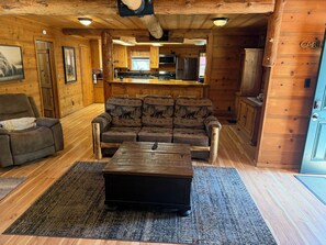 Ein Holzblockhaus-Innenraum mit einer Sofagarnitur, einem Couchtisch und einer Küchenzeile.