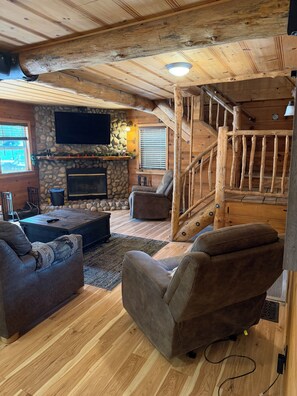 Ein gemütliches Blockhaus-Interieur mit Kamin aus Stein, Holzboden, einer komfortablen Sitzecke und einer Treppe.