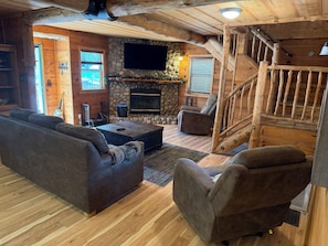 Ein gemütliches Wohnzimmer mit Kamin aus Stein, einem Flachbildfernseher, einer Holztreppe und einem Sofa.
