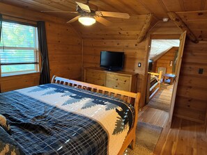 Une chambre dans une cabane en bois, avec un lit, un téléviseur posé sur une commode et un ventilateur de plafond.