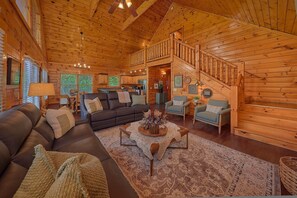 A log cabin interior with a living room, dining area, kitchen, and a staircase. - Smoky Mountain Lodge | Sleeps 17, Theater, Hot Tub, Game Room, King Suites + Free Attraction Tickets (Pigeon Forge)