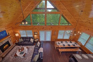 A spacious cabin with a high ceiling, a fireplace, a dining area, and multiple windows. - Smoky Mountain Lodge | Sleeps 17, Theater, Hot Tub, Game Room, King Suites + Free Attraction Tickets (Pigeon Forge)