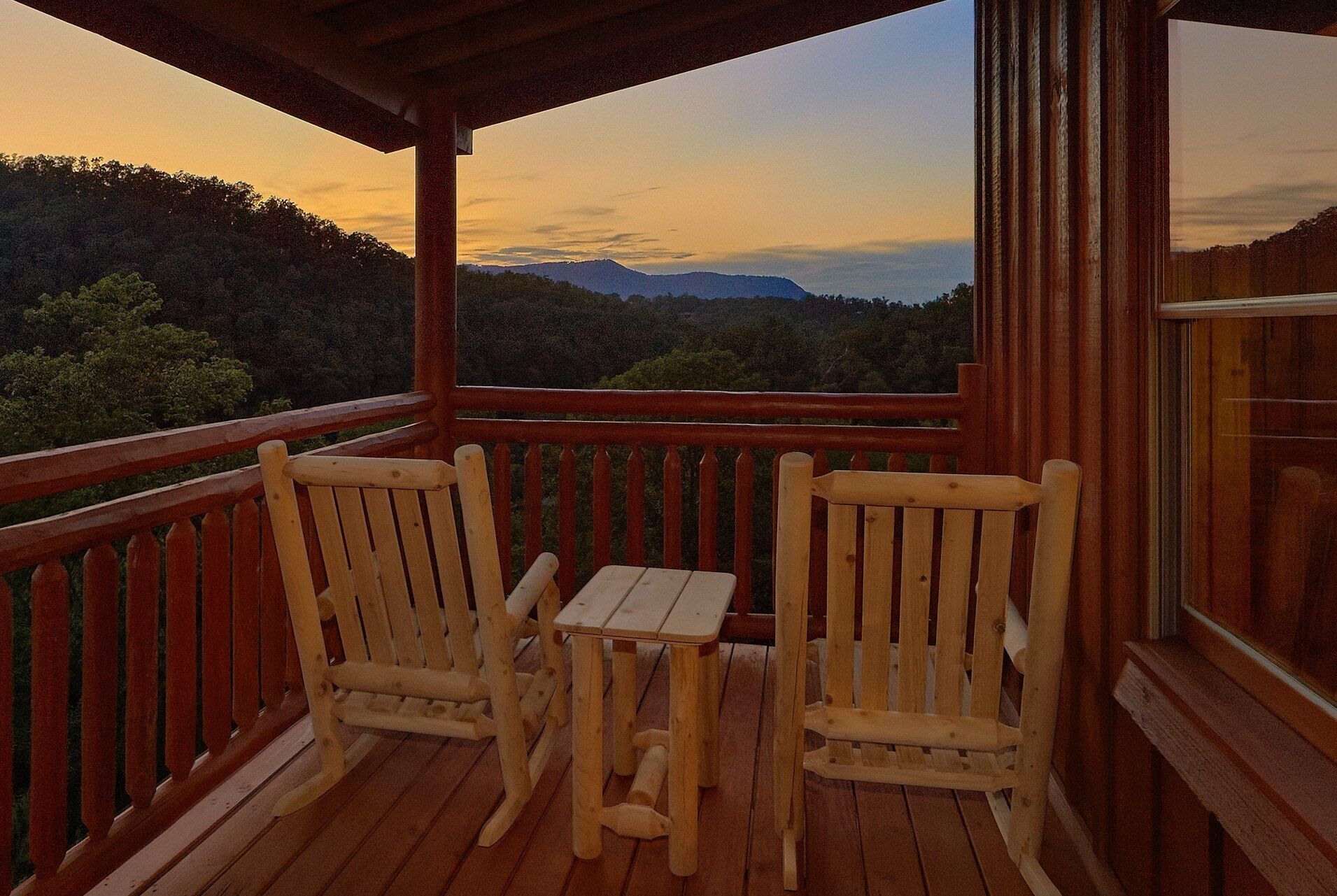 Terraza de madera con dos sillas y una mesa, con vista a un paisaje boscoso.