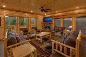 A log cabin interior with a fireplace, wooden furniture, and a television. - Splashin On Majestic Mountain | Private Pool, Theater, Smoky Mtn Views + Free Attraction Tickets (Sevierville)