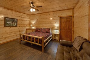 A wooden cabin bedroom with a bed, two bedside tables, a ceiling fan, and a door. - Splashin On Majestic Mountain | Private Pool, Theater, Smoky Mtn Views + Free Attraction Tickets (Sevierville)