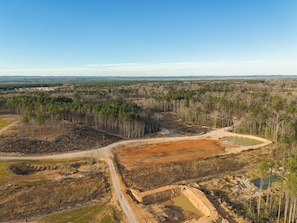 An aerial view of a forested area with a dirt road and a large open excavation site.