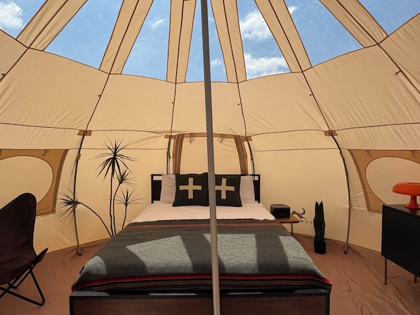 A tent with a bed, a chair, a table, and a plant.