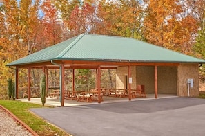 A covered pavilion with a flat roof, outdoor seating, and a stone wall. - Sugar and Spice | Mtn Views, Hot Tub, Game Room, Sleeps 10, King Suites + Free Attraction Tickets (Sevierville)