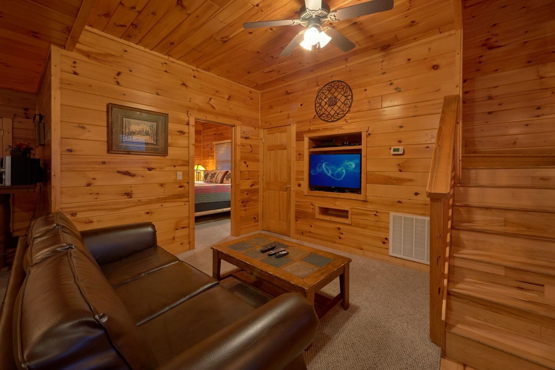 A wooden cabin interior with a leather couch, a television, and a ceiling fan.
