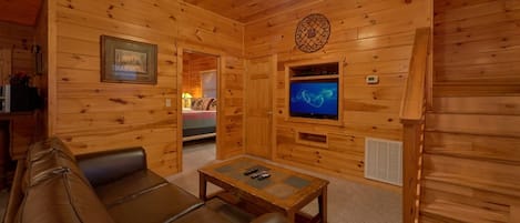 A wooden cabin interior with a leather couch, a television, and a ceiling fan.
