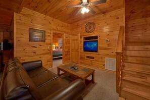 Een houten cabin met een leren bank, een televisie en een plafondventilator.