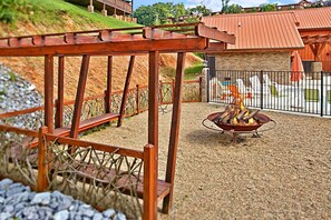 A wooden pergola structure, a fire pit, and a fenced outdoor area with a view of a building in the background. - Sundaze | Hot Tub, King Suites, Fire Pit, Pigeon Forge, Resort Pool + Free Attraction Tickets (Pigeon Forge)