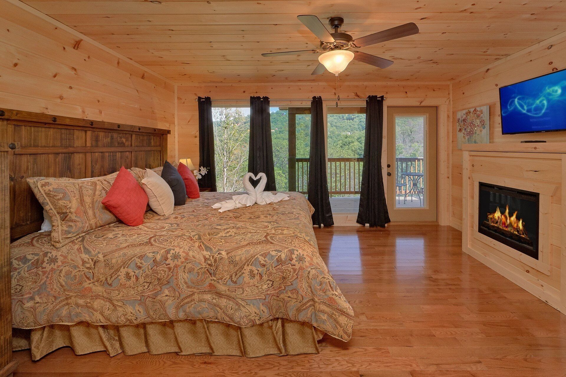 Une chambre à coucher dans un chalet en bois, avec un lit, une cheminée, un ventilateur de plafond et un téléviseur.
