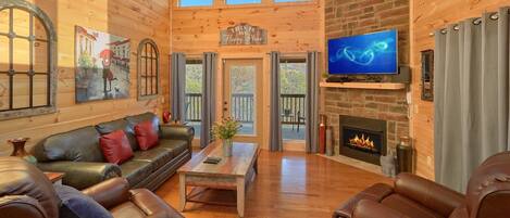 A cozy living room with a leather sofa, a coffee table, a fireplace, and a television.
