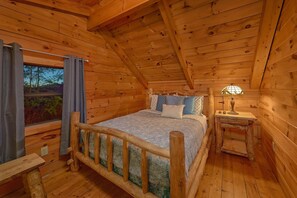 A cozy wooden cabin bedroom with a bed, bedside table, lamp, and a window with curtains. - The Waterlog | Indoor Pool, Mtn Views, Hot Tub, Near Dollywood, Game Room + Free Attraction Tickets (Pigeon Forge)