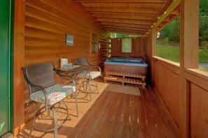 A wooden deck with a hot tub, two chairs, and a table. - Whispering Pond | Hot Tub, Resort Pool, Fireplace + Free Attraction Tickets (Sevierville)