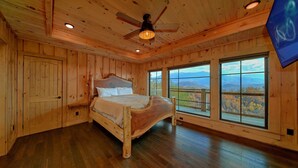 Ein Schlafzimmer aus Holz mit einem Bett, einem Deckenventilator und großen Fenstern mit Blick auf die Berge.