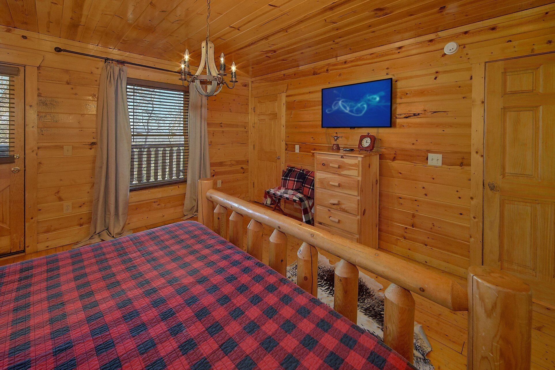 Habitación de cabaña de madera con una cama, televisor, cómoda y ventana con persianas.