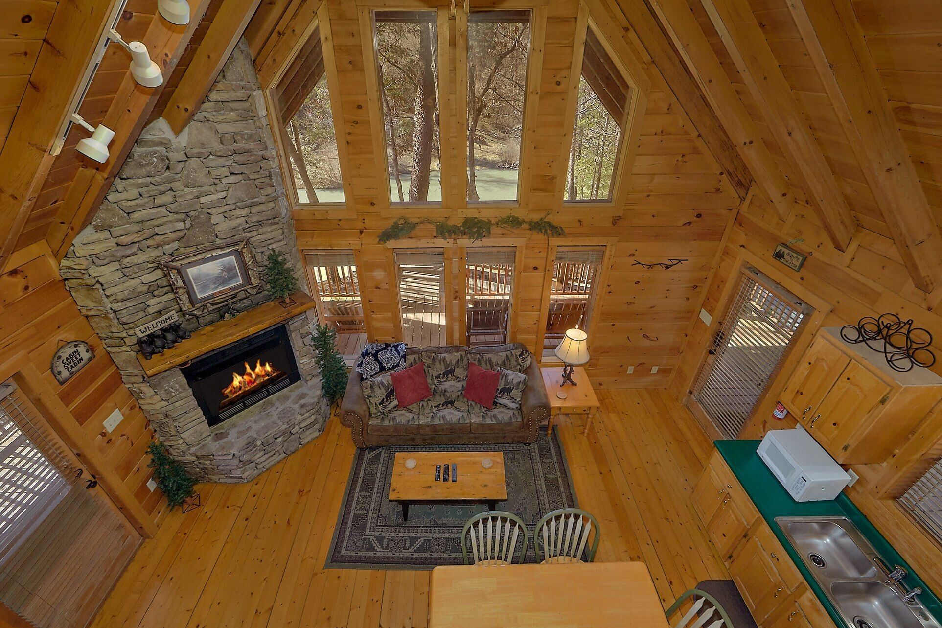 A cabin interior with a stone fireplace, wooden walls, a dining area, and a view of the outdoors.