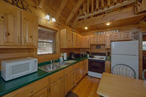 A wooden cabin-style kitchen with a microwave, sink, stove, and a 'WELCOME' sign. - Heavenly-RAE Cabin Rental (Wears Valley)