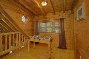 Ein Zimmer mit Holzboden, einem Kicker, einem fenster mit Vorhängen und einer Treppe.