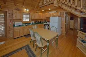 A wooden cabin interior with a kitchen, dining area, and a staircase. - Heavenly-RAE Cabin Rental (Wears Valley)