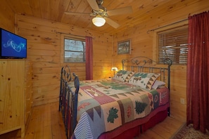 Ein Schlafzimmer einer Holzhütte mit einem Bett, einem Fernseher und einem Deckenventilator.
