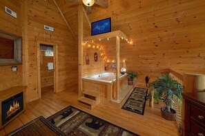 Ein Holzblock-Interieur mit Holzboden, Kamin, großem Fenster, Holzbalkendecke und einem Badezimmer mit Badewanne.