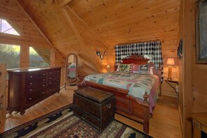 A cozy attic bedroom with a wooden ceiling, a large bed with a quilt, a dresser, a chest of drawers, and a mirror. - A Romantic Hilltop | Hot Tub | Pool Table (Sevierville)