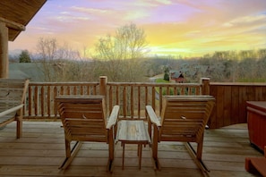 Eine Holzterrasse mit zwei Stühlen und einem Tisch, mit Blick auf eine Landschaft mit Bäumen und Häusern.