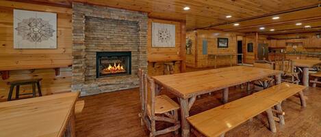 Un interior rústico con chimenea de piedra, mesas y bancos de madera, y una zona de cocina.