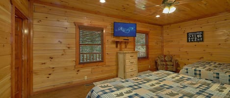 Een houten kamer met twee bedden, een plafondventilator, een televisie en een wandplank.