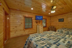 A wooden cabin room with two beds, a ceiling fan, a television, and a wall-mounted shelf. - The Big Lebowski | Sleeps 46, Indoor Pool, Theater, Hot Tub, Arcade + Free Attraction Tickets (Pigeon Forge)