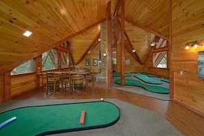 Ein Dachzimmer mit Holzbalken, einem Billardtisch und einem Essbereich mit Stühlen und Tisch.
