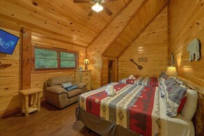 A cozy log cabin room with a bed, a sofa, a television, and a window with blinds. - The Big Lebowski | Sleeps 46, Indoor Pool, Theater, Hot Tub, Arcade + Free Attraction Tickets (Pigeon Forge)