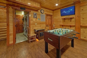 A room with wooden walls, a foosball table, a clock, and a television. - The Big Lebowski | Sleeps 46, Indoor Pool, Theater, Hot Tub, Arcade + Free Attraction Tickets (Pigeon Forge)