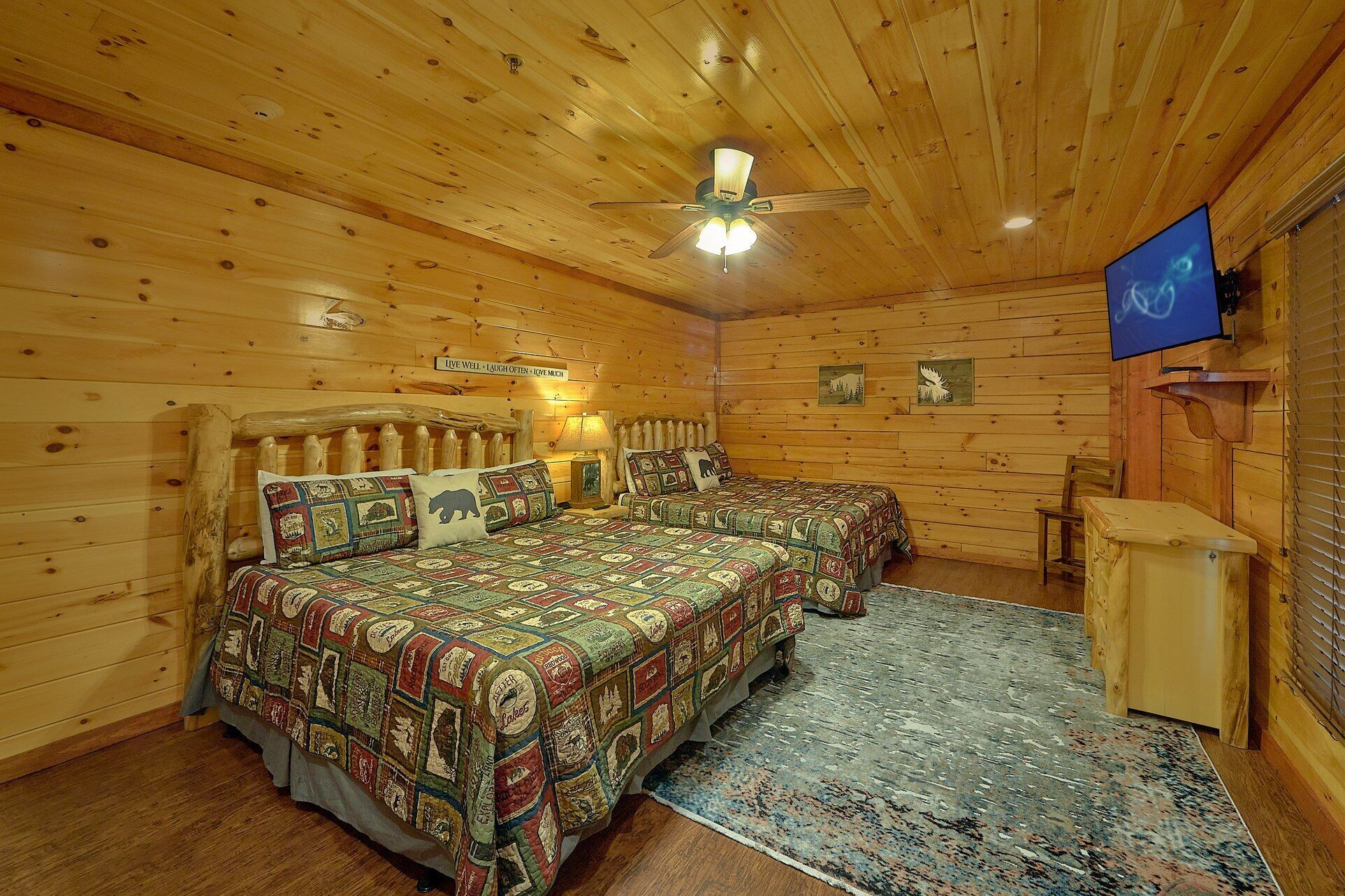 Ein rustikal eingerichtetes Zimmer mit Holzbalkendecke, einem Bett mit Quilzudecke, einem Fernseher und einem kleinen Schreibtisch.