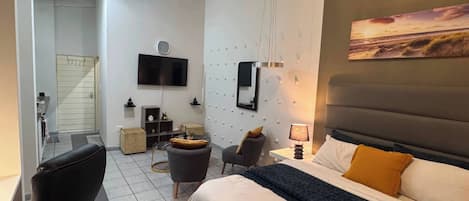 A modern bedroom with a large bed, a TV mounted on the wall, and a painting above the bed.