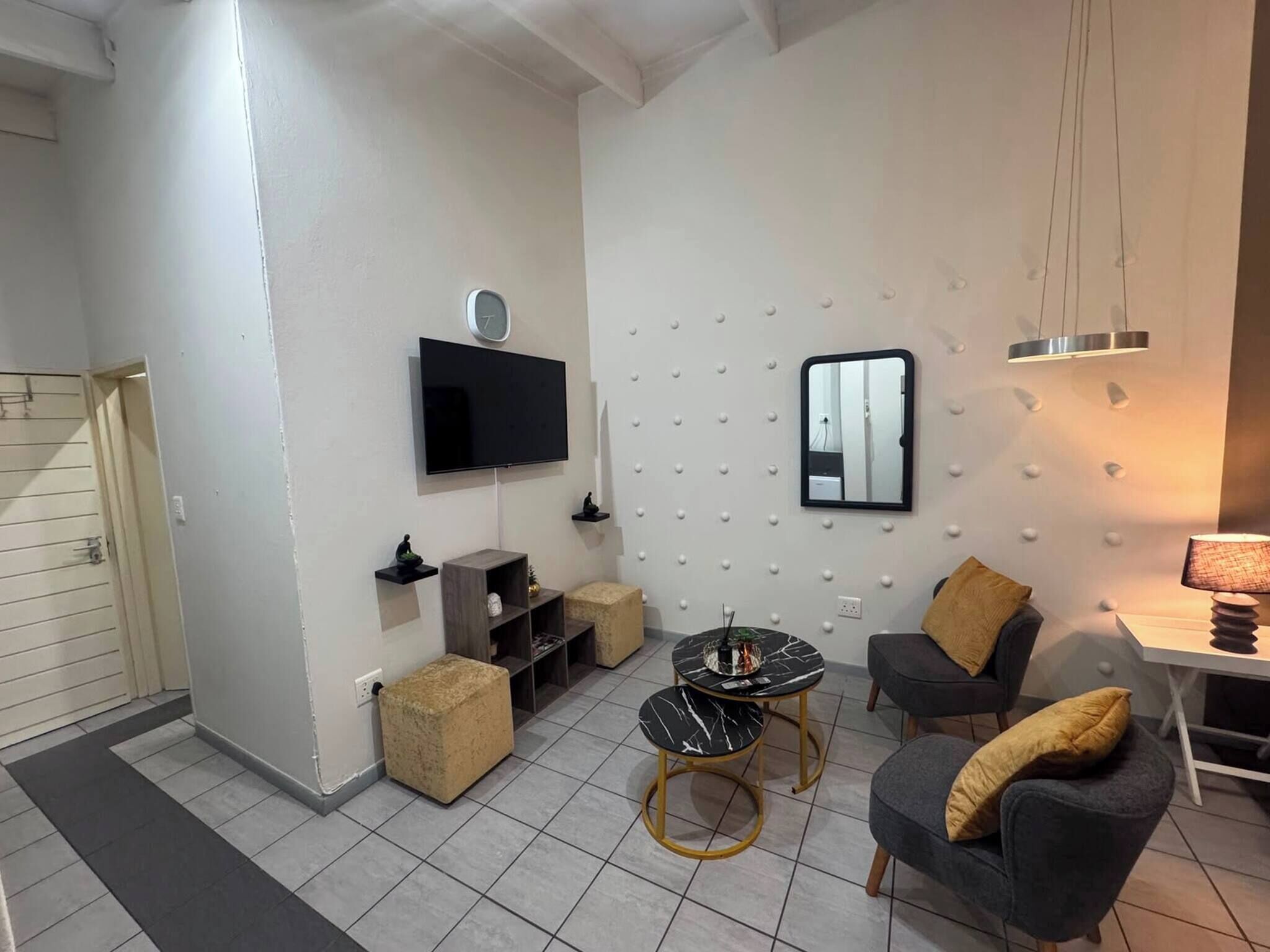 A modern living room with a flat-screen TV, a round coffee table, and two armchairs.