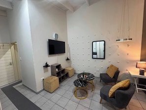 Un salon moderne avec un téléviseur à écran plat, une table basse ronde et deux fauteuils.