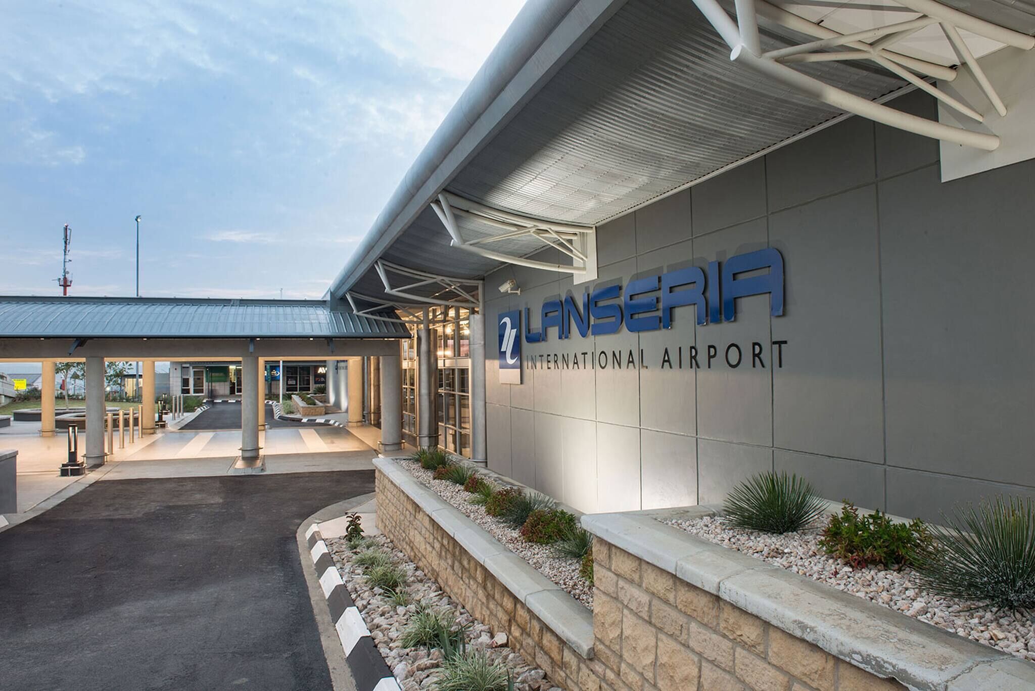 An airport terminal with a clear entrance, a sign reading 'LANSERIA INTERNATIONAL AIRPORT', and a covered walkway.