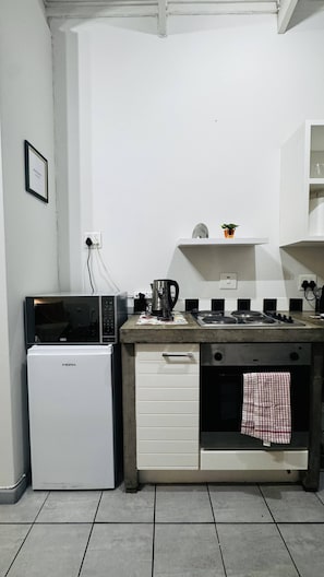 A compact kitchenette with a refrigerator, microwave, stove, and a small shelf above the counter. - Experience Elevated Living in Dainfern's Panorama Suite (Johannesburg)